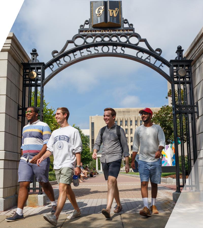 4 male students in shorts under the GW archway with letters GW over their heads, outdoors